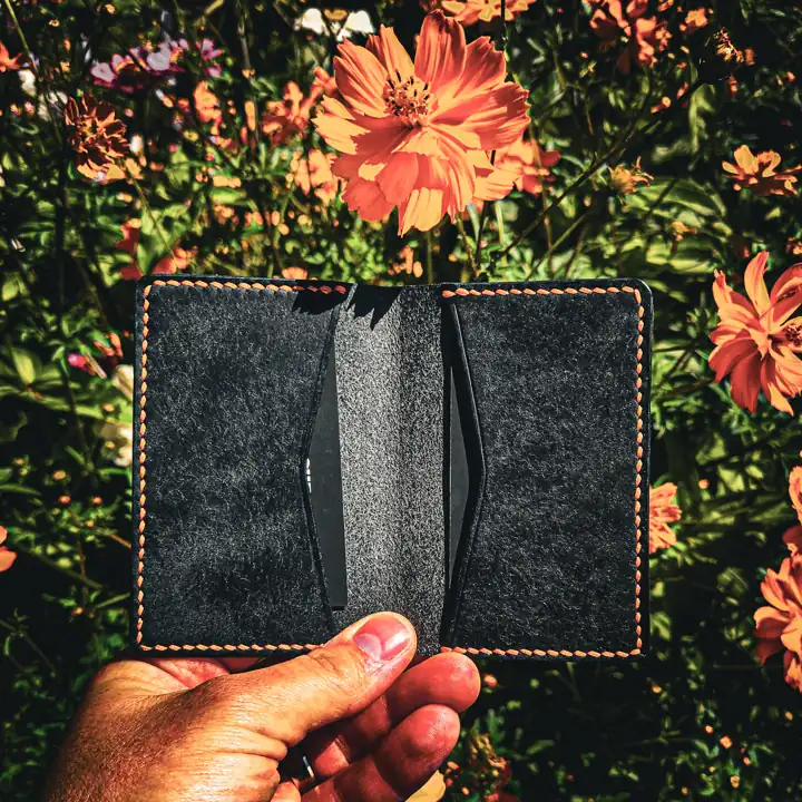Card wallet held open in the flower garden — black interior, tan saddle stitch — Rogue Artisan, East Vancouver