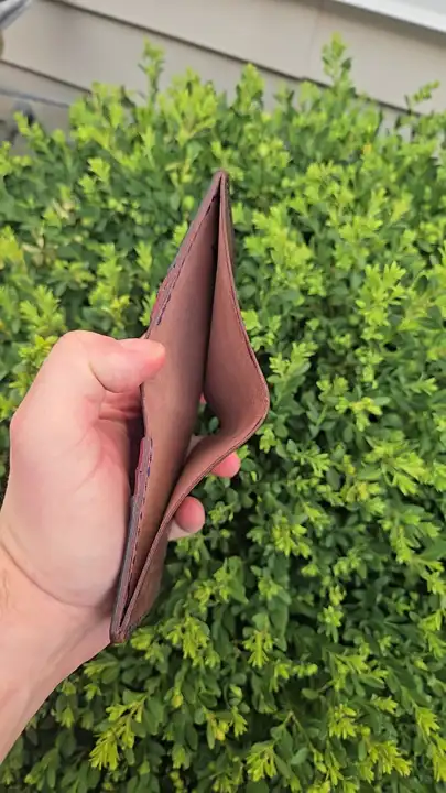Oxblood bifold held open against the hedge — Rogue Artisan, East Vancouver